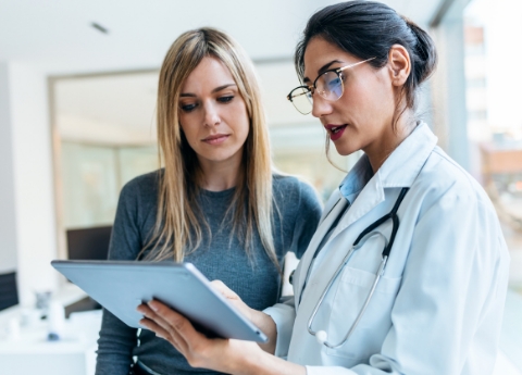A physician holding a tablet while discussing medical information with a patient